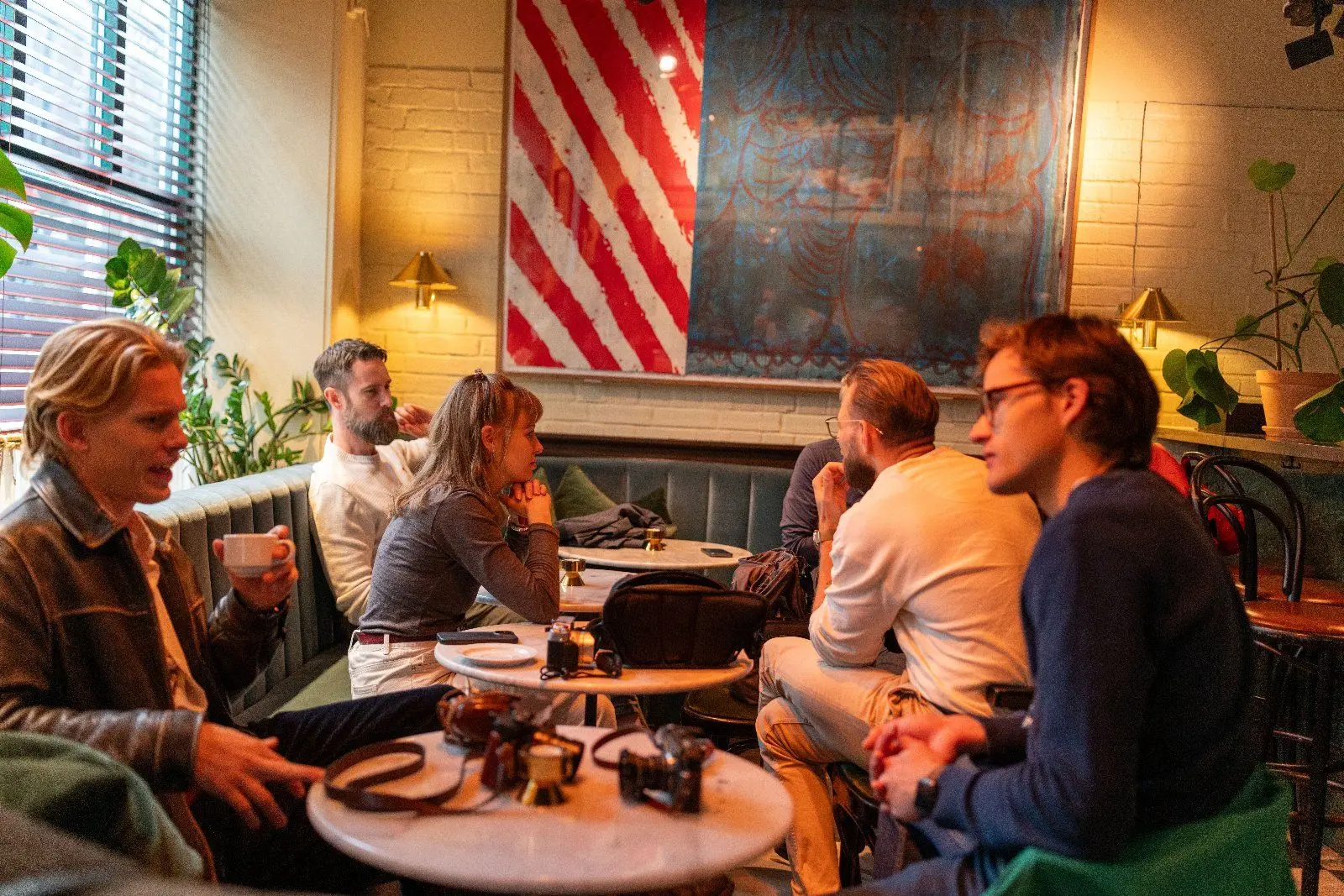 Guests sit around marble tables with film cameras and coffee, in front of a red and white striped artwork.