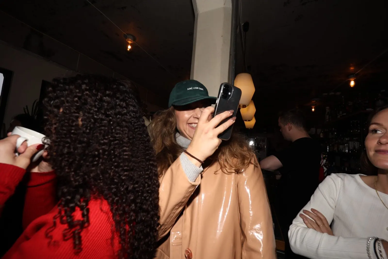 A guest in a green cap holds up a phone to take a photo in the busy room.