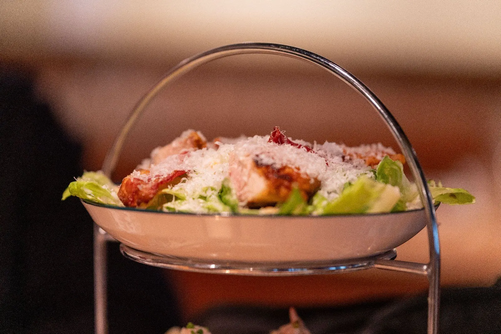 A chicken salad with parmesan sits on a tiered stand in warm light.