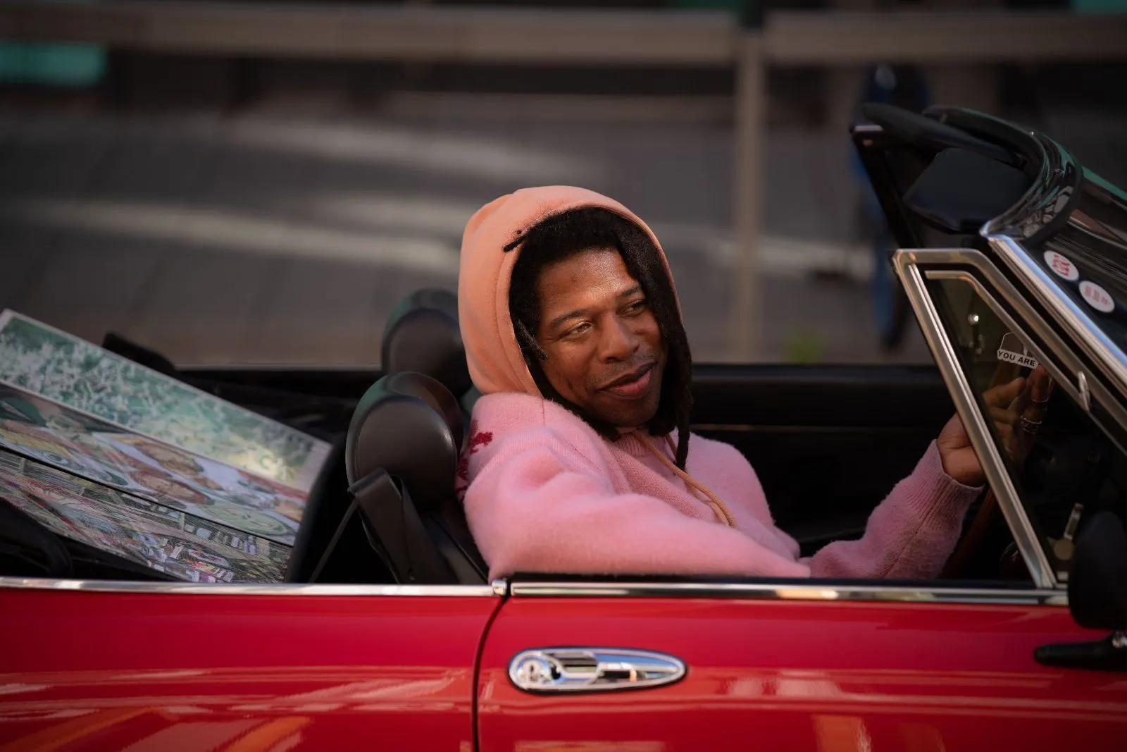 A smiling guest in a pink hoodie sits in the passenger seat of a red convertible parked on the street.
