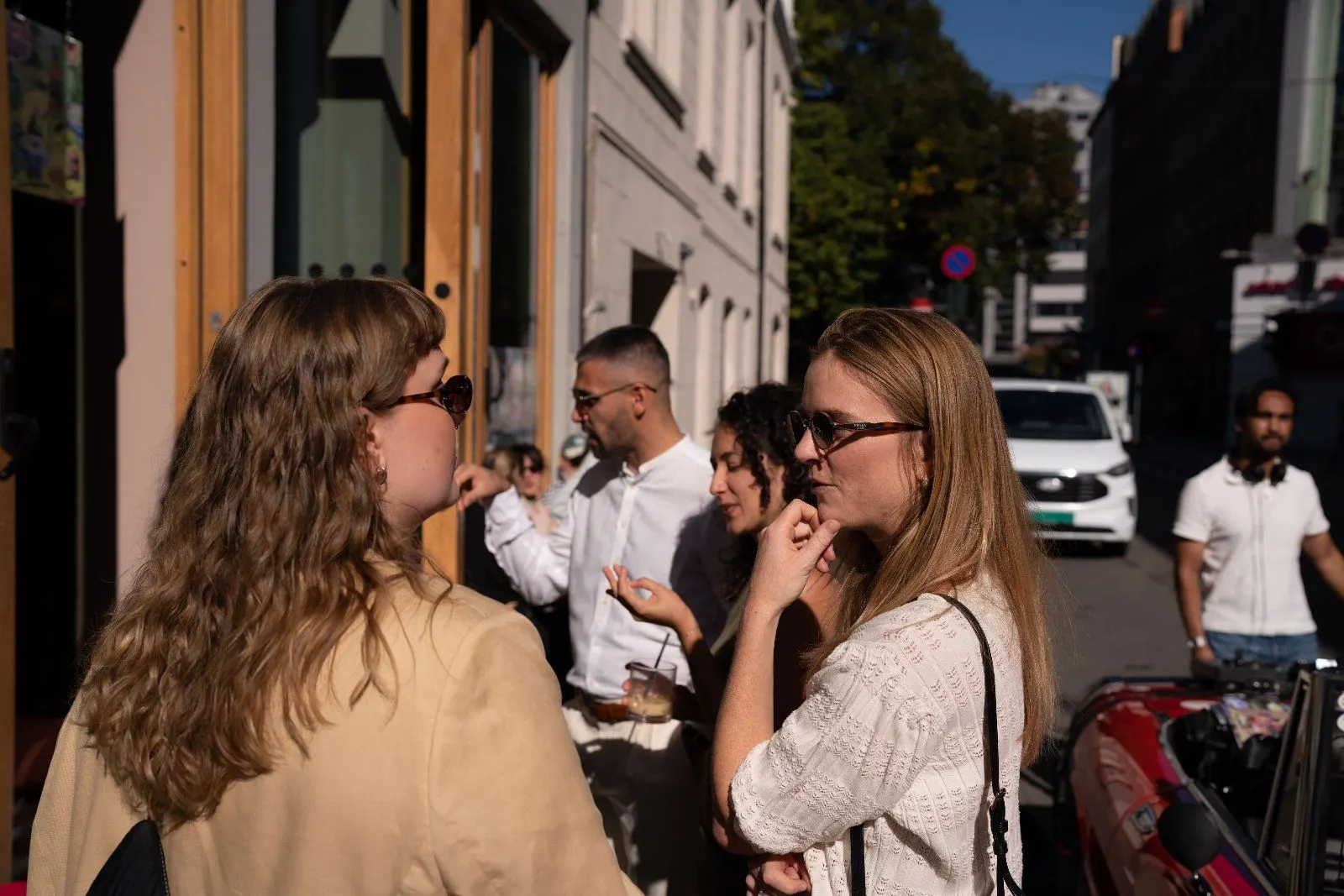 Two guests talk on the pavement while others mingle by the café doors behind them.