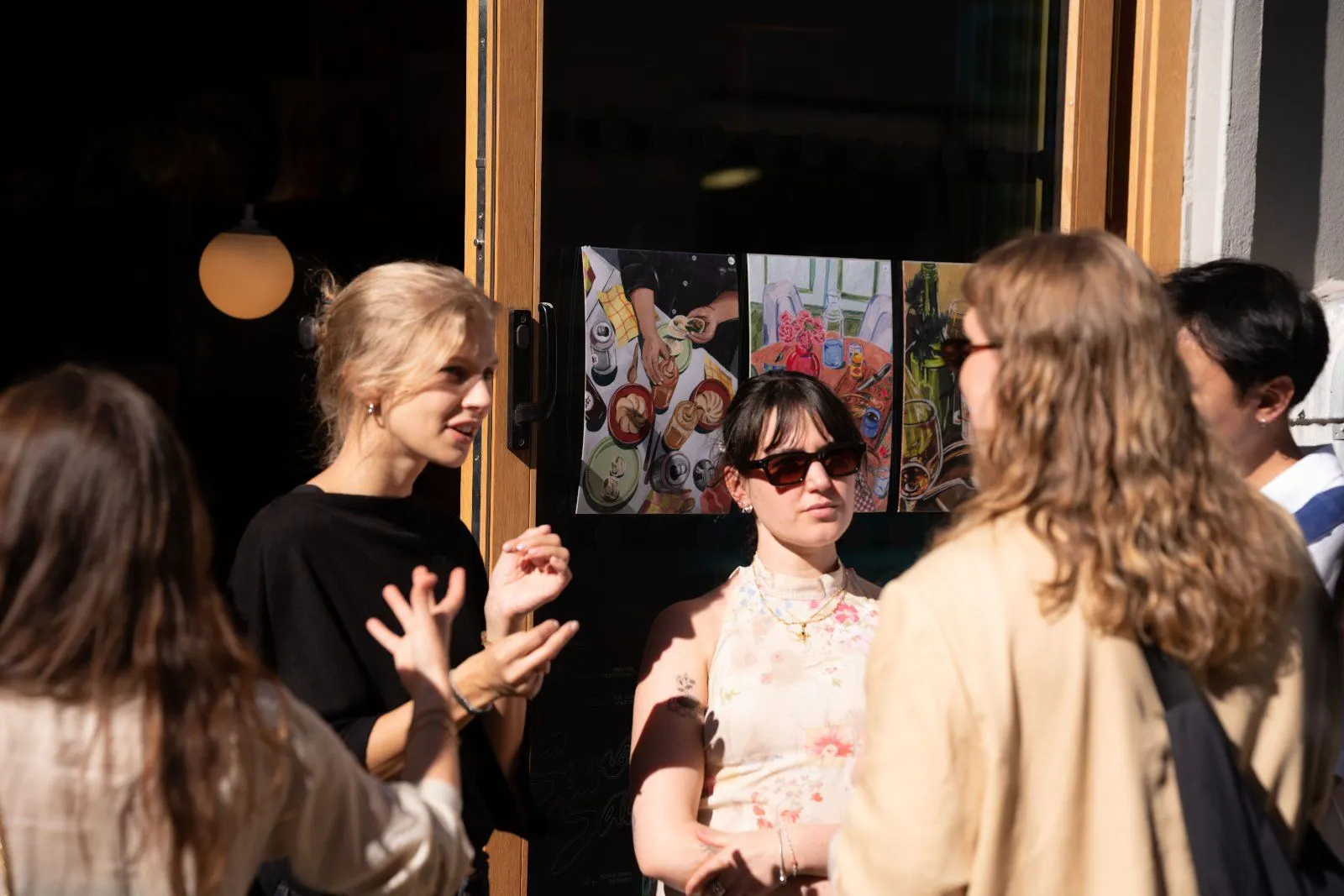Three guests lean in to talk in the shade of the doorway, with a colourful artwork behind them.