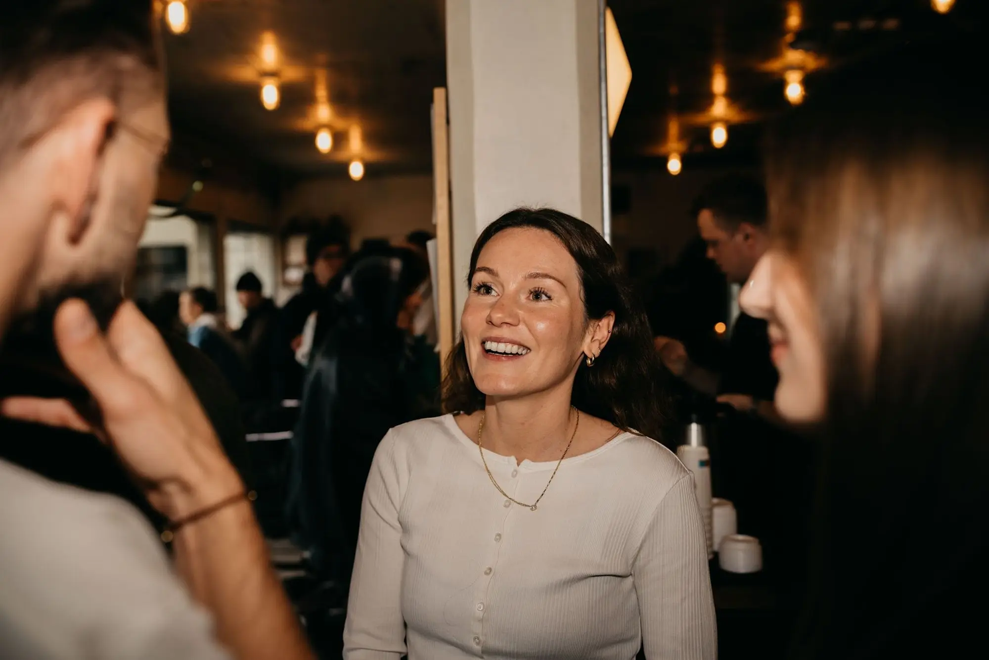 A smiling woman in a cream cardigan listens to the conversation around her.