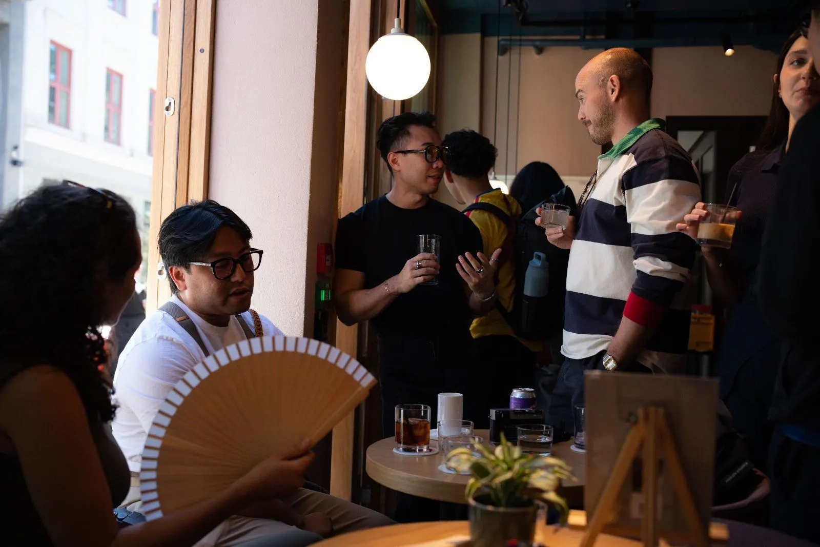 Guests sit at a small table inside, one fanning herself with a wooden hand fan.