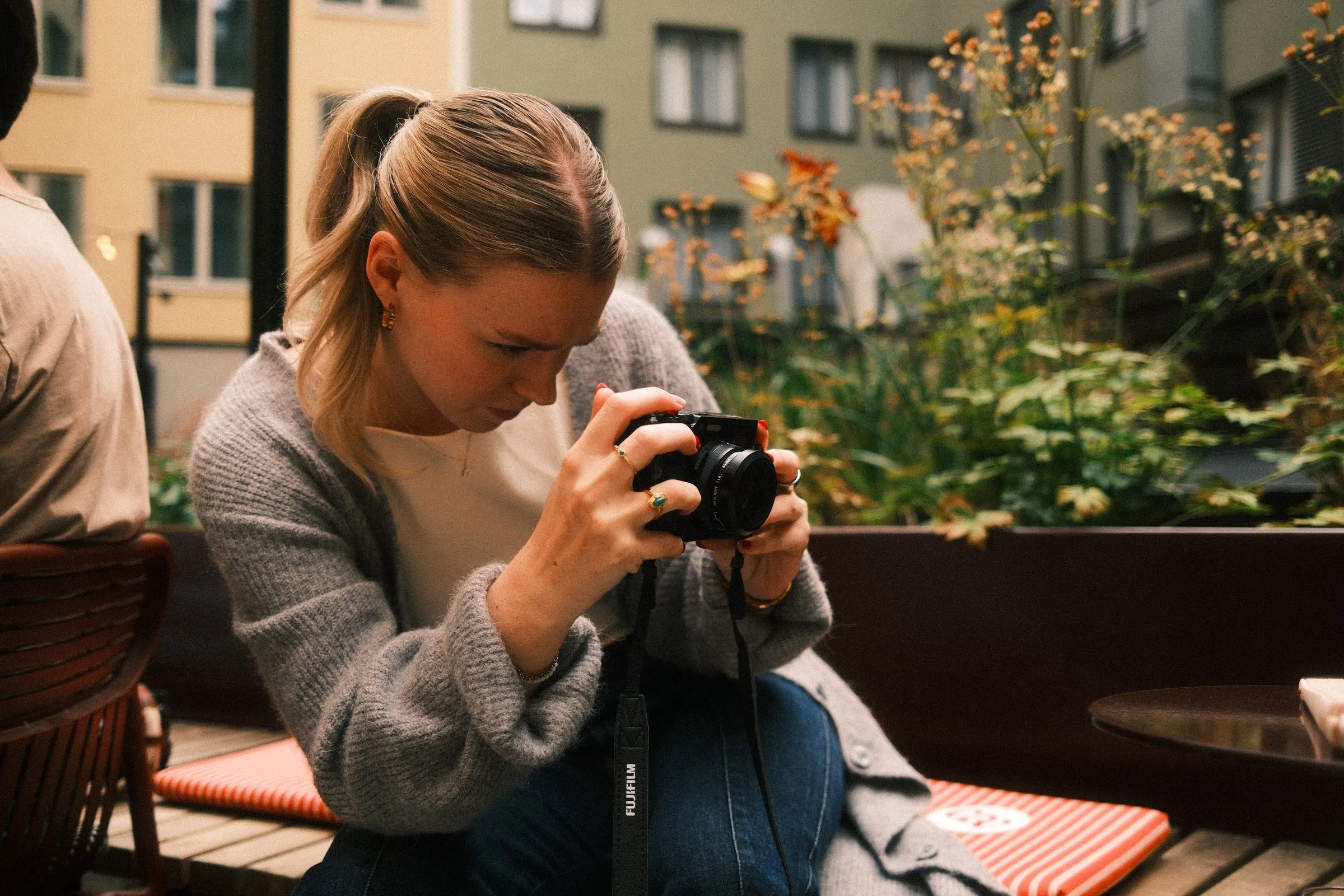 A guest in a grey cardigan lines up a shot with a compact camera among the courtyard planters.